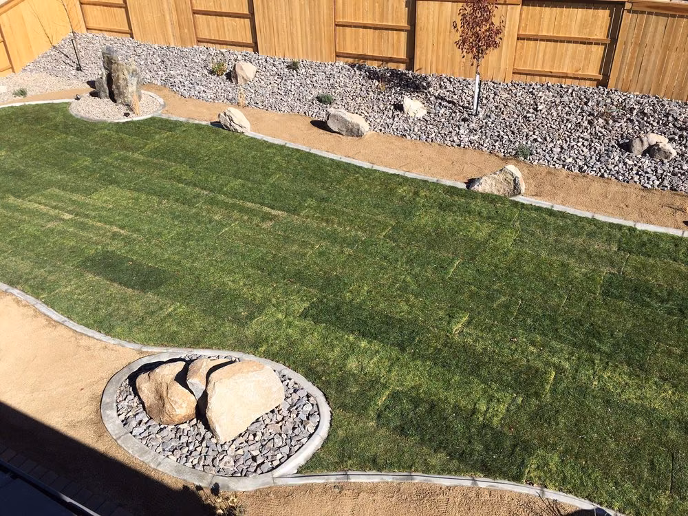 A sloped lawn bordered by a gravel and boulder bed along a wood fence